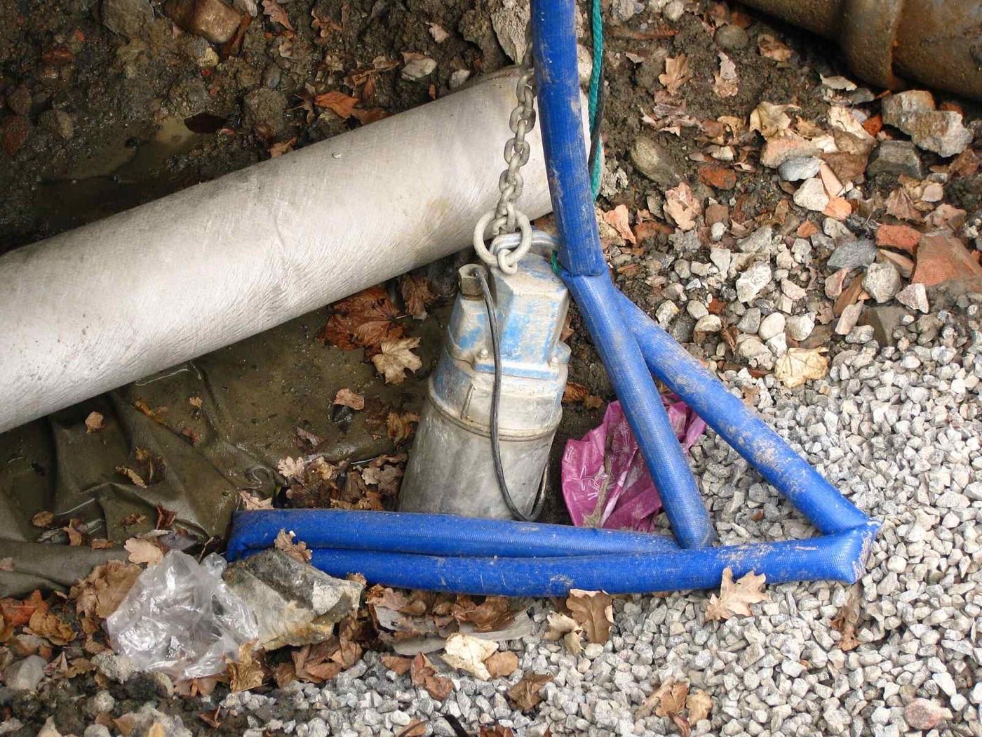 Pompe immergée de chantier suspendue par une chaîne avec tuyau bleu raccordé, aucune inscription lisible